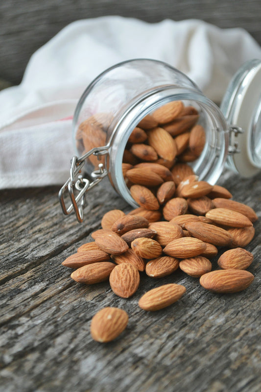 Almonds spilling from a glass storage jar onto a wooden table