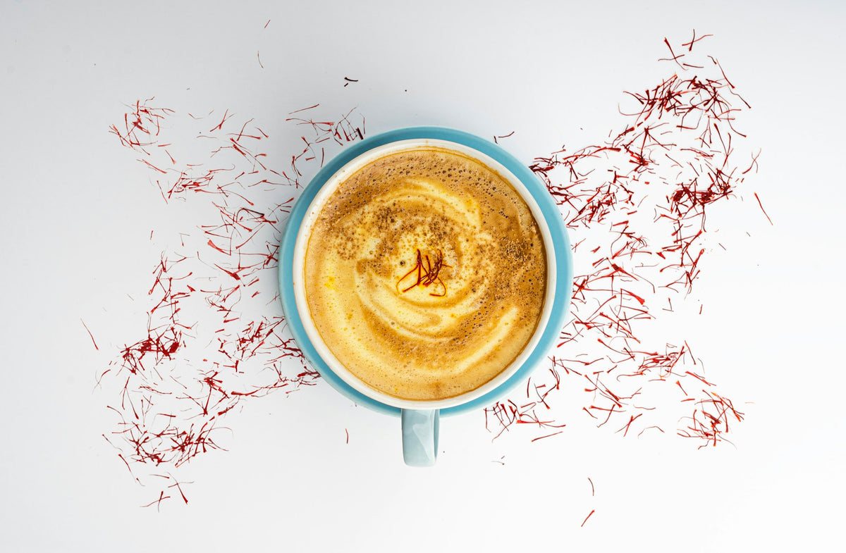 A cup of saffron milk surrounded by loose saffron threads