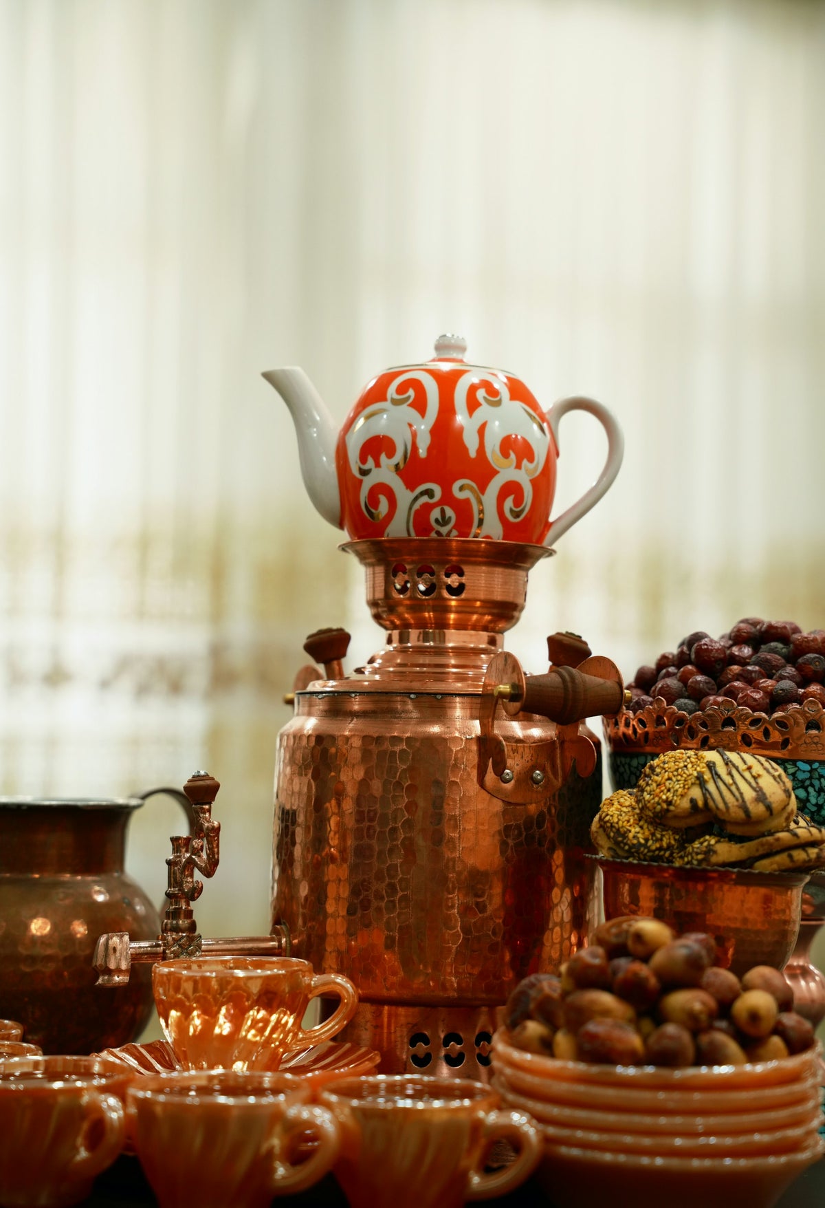 A copper samovar with a teapot on top, beside dried fruit and sweets