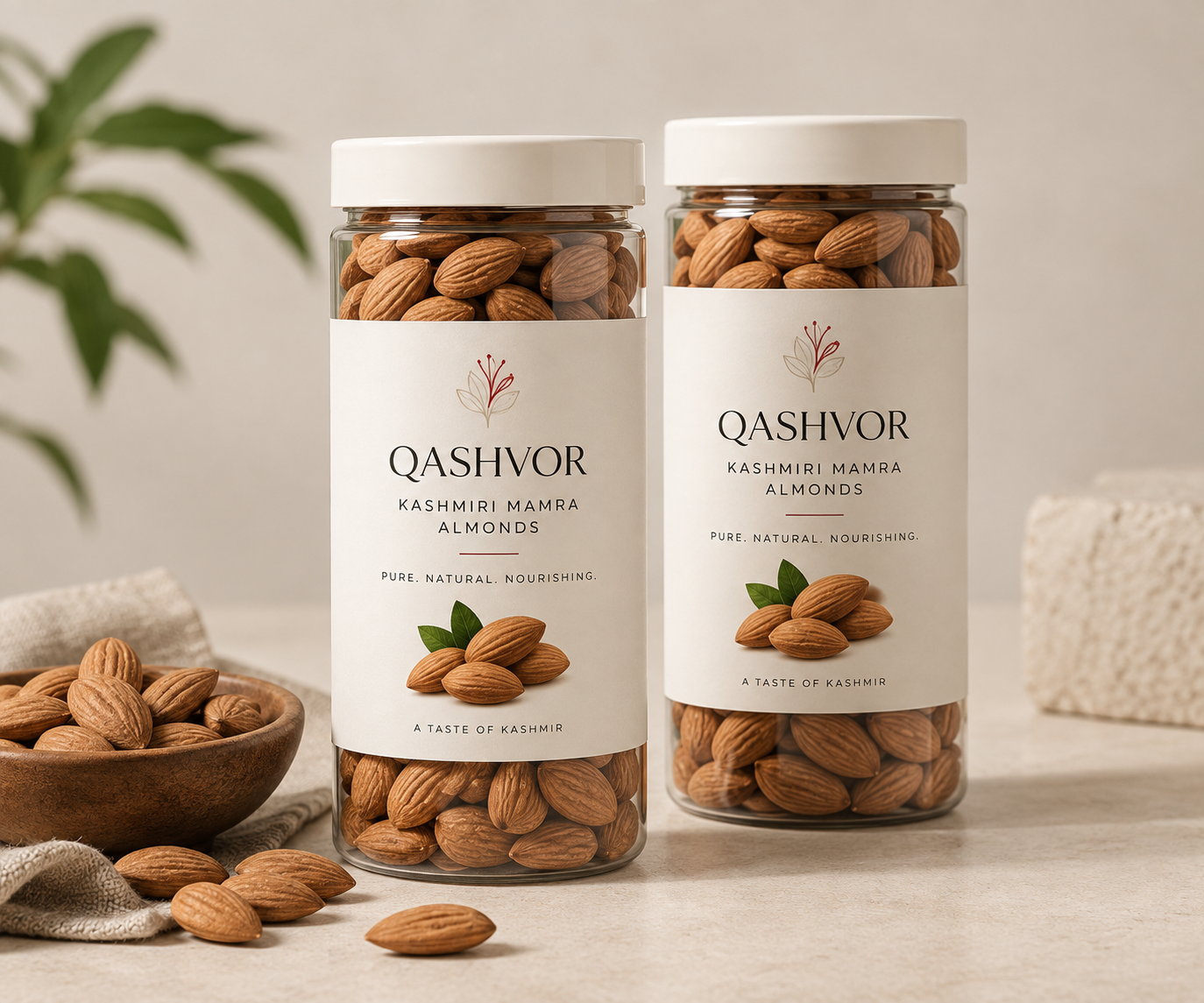 Two jars of Qashvor Kashmiri Mamra almonds beside a wooden bowl of almonds